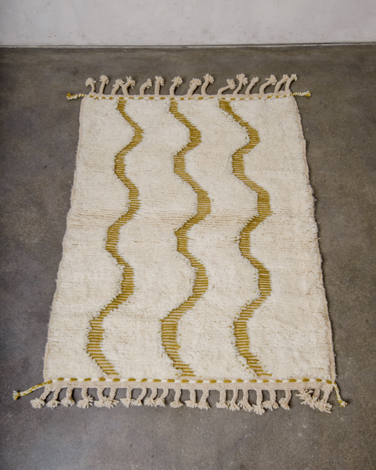 Small wool Berberlin Beniourain rug in cream featuring woven olive green waves, laying on concrete floor.